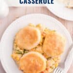 A plate of chicken pot pie casserole topped with three biscuits, beside a fork, on a wooden table.