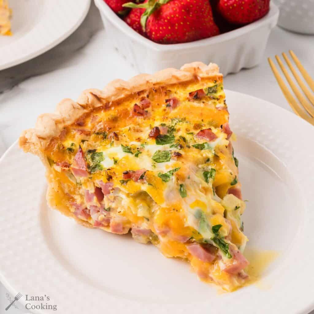 A slice of ham and cheese quiche on a white plate.