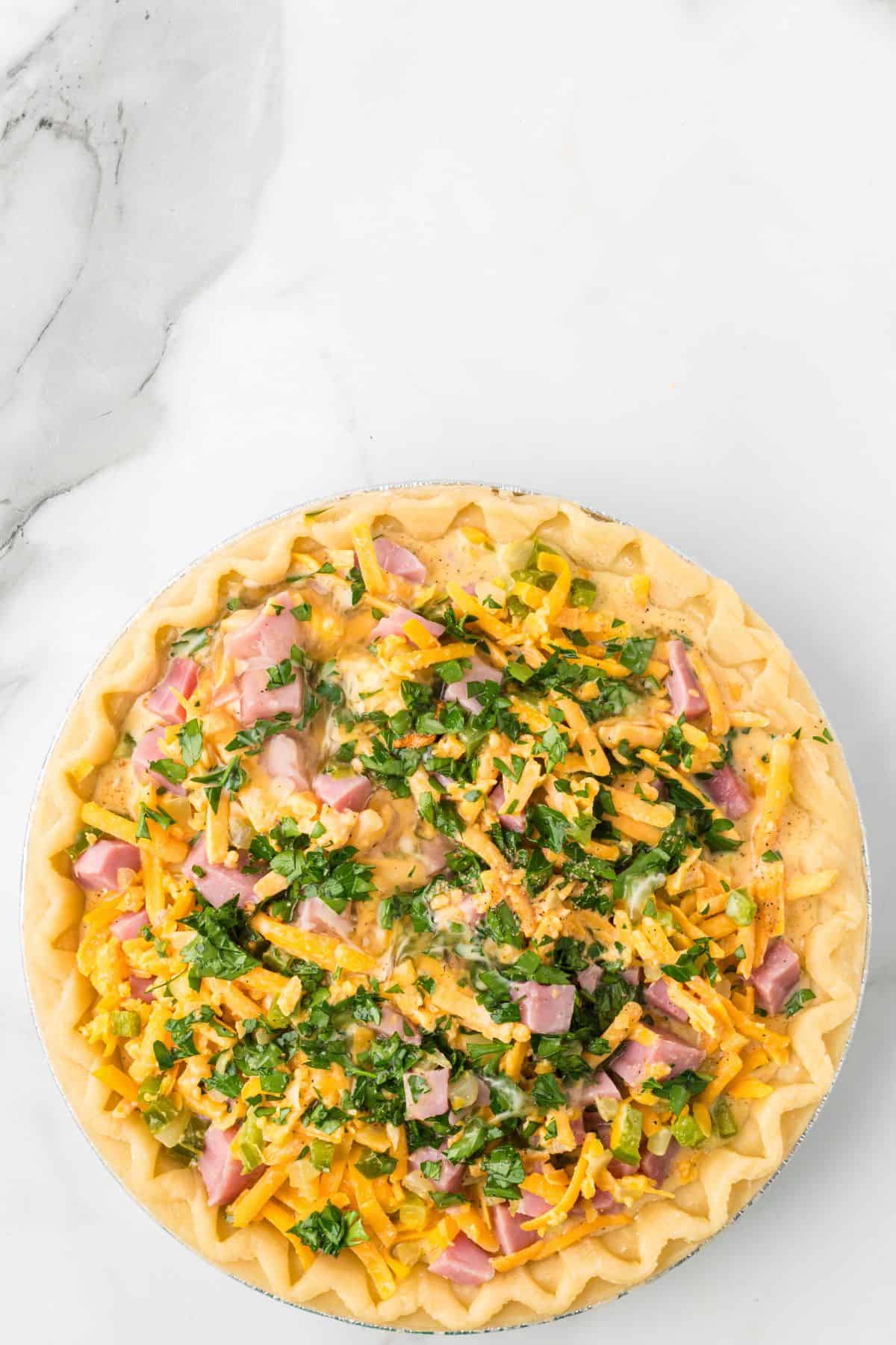 Egg mixture after being poured into the pie shell with the ham, vegetables, and cheese.