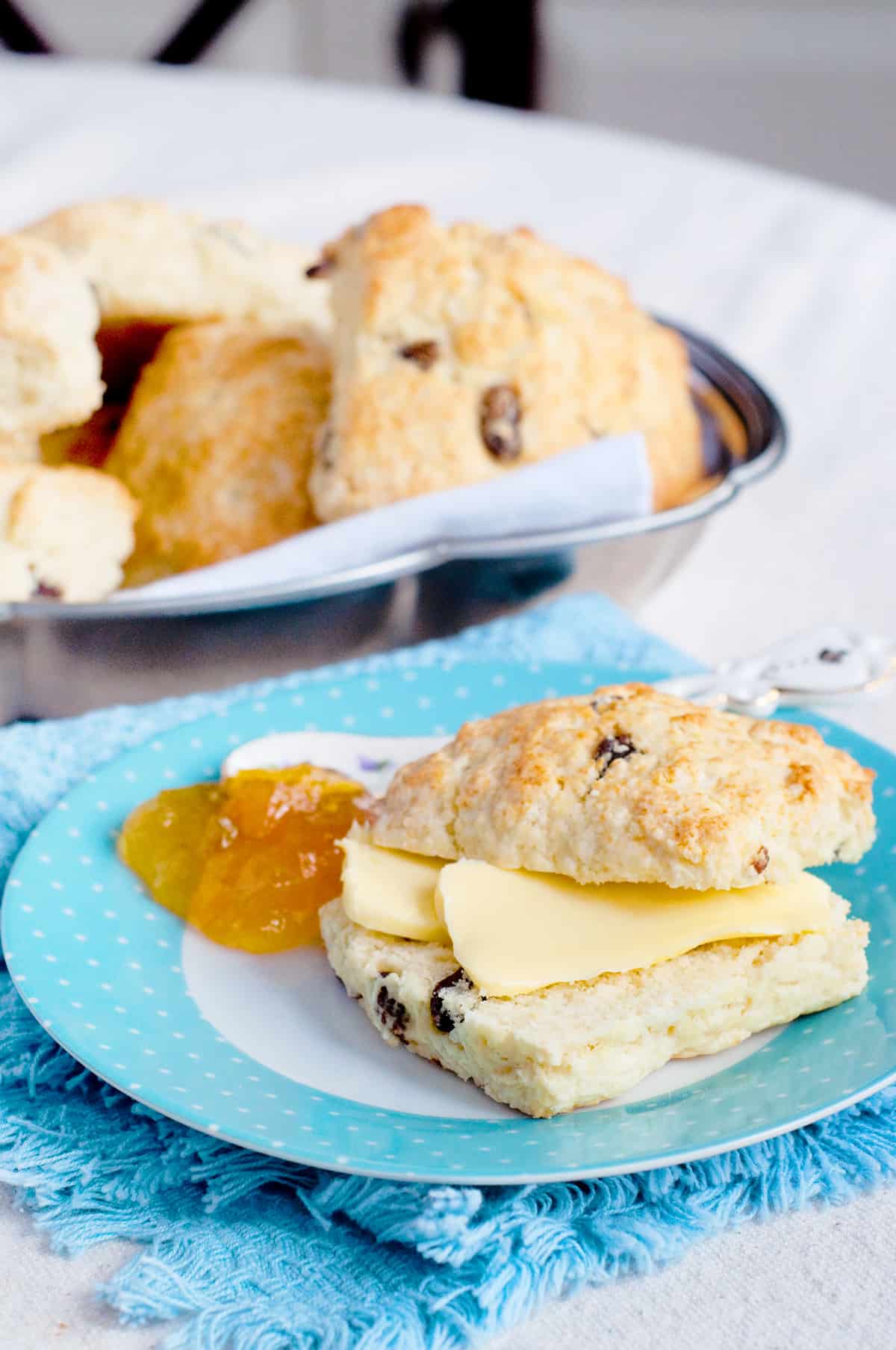 A scone with butter and jam on a decorative plate.