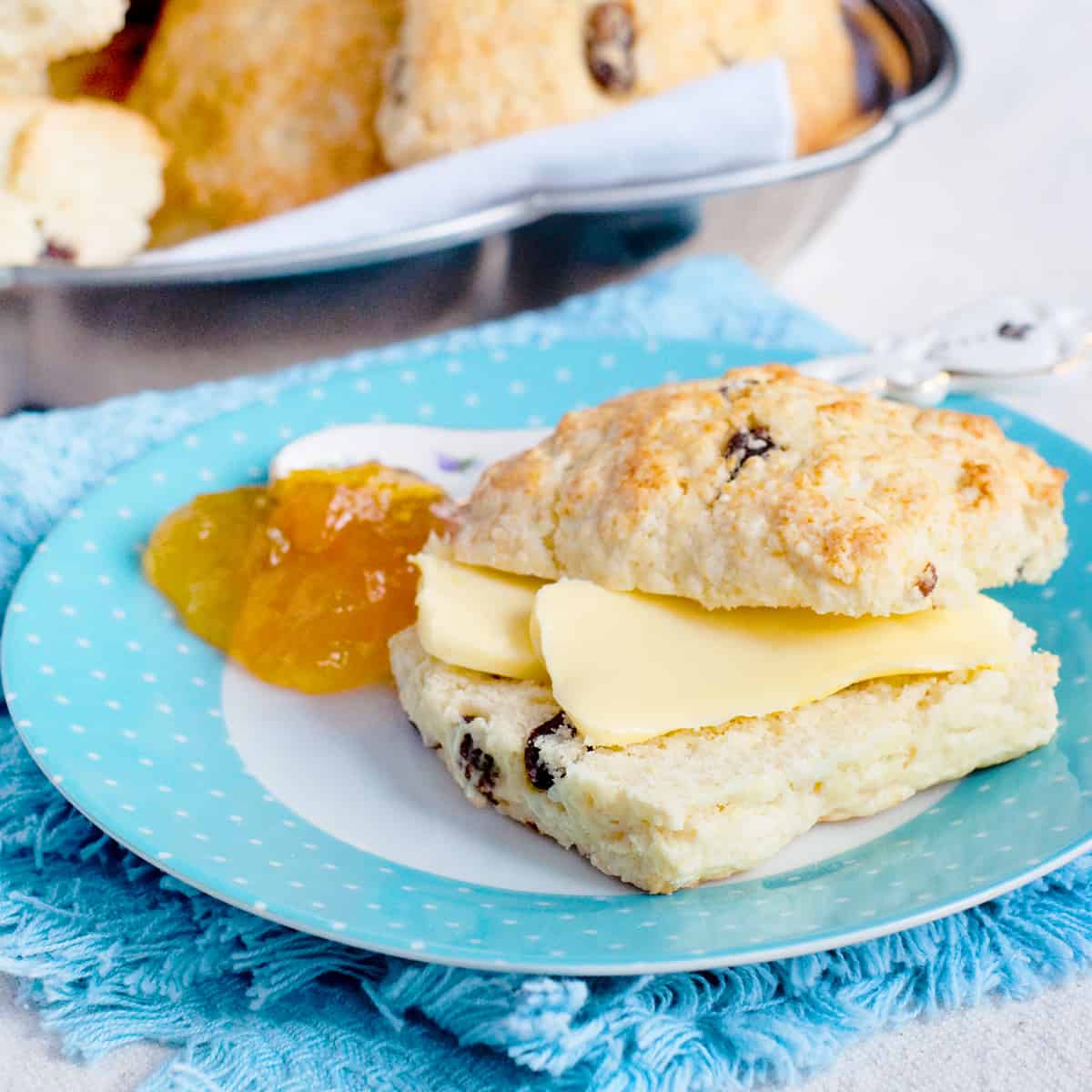 A scone with butter and jam on a decorative plate.