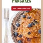 Plate of oatmeal blueberry pancakes topped with fresh blueberries and nuts, with a fork on the side.