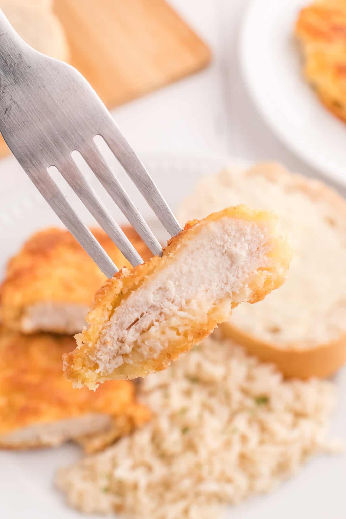 Finished chicken breast on a white plate with rice and roll on the side.