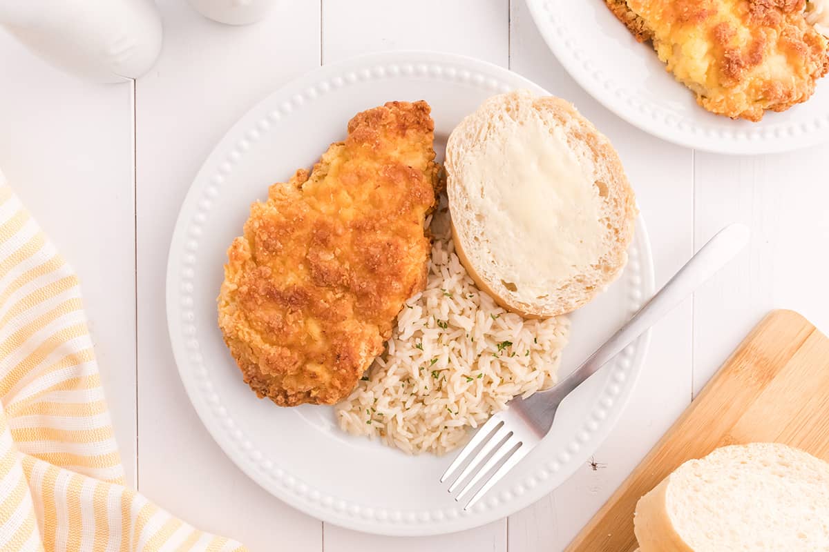 Finished chicken breast on a white plate with rice and roll on the side.