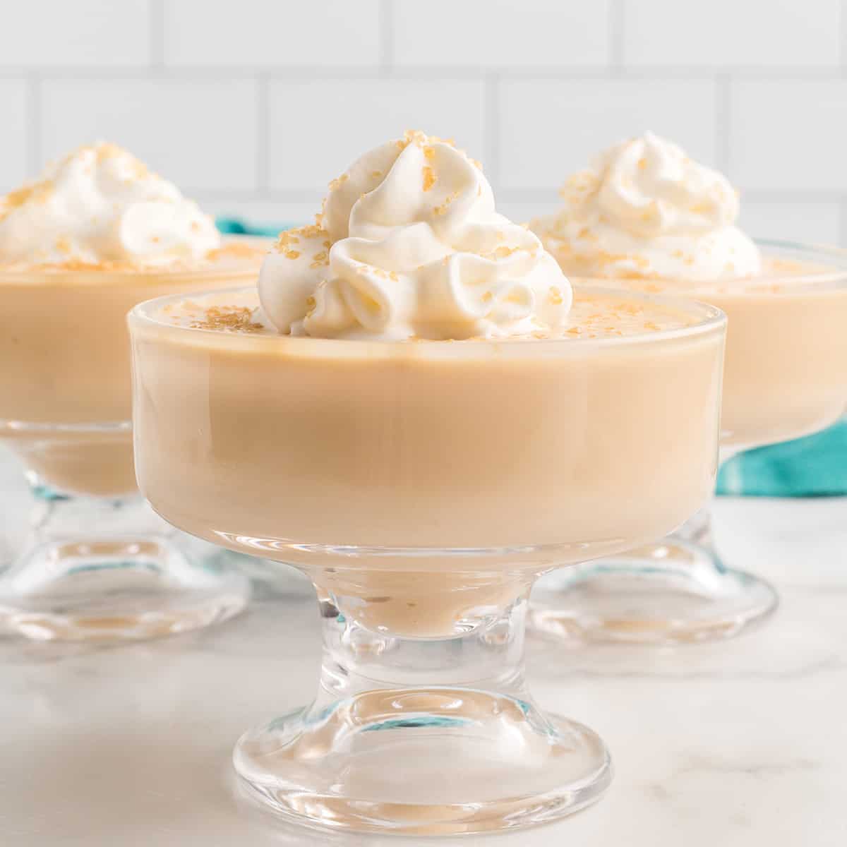 Three dishes filled with butterscotch pudding topped with whipped cream and turbinado sugar.