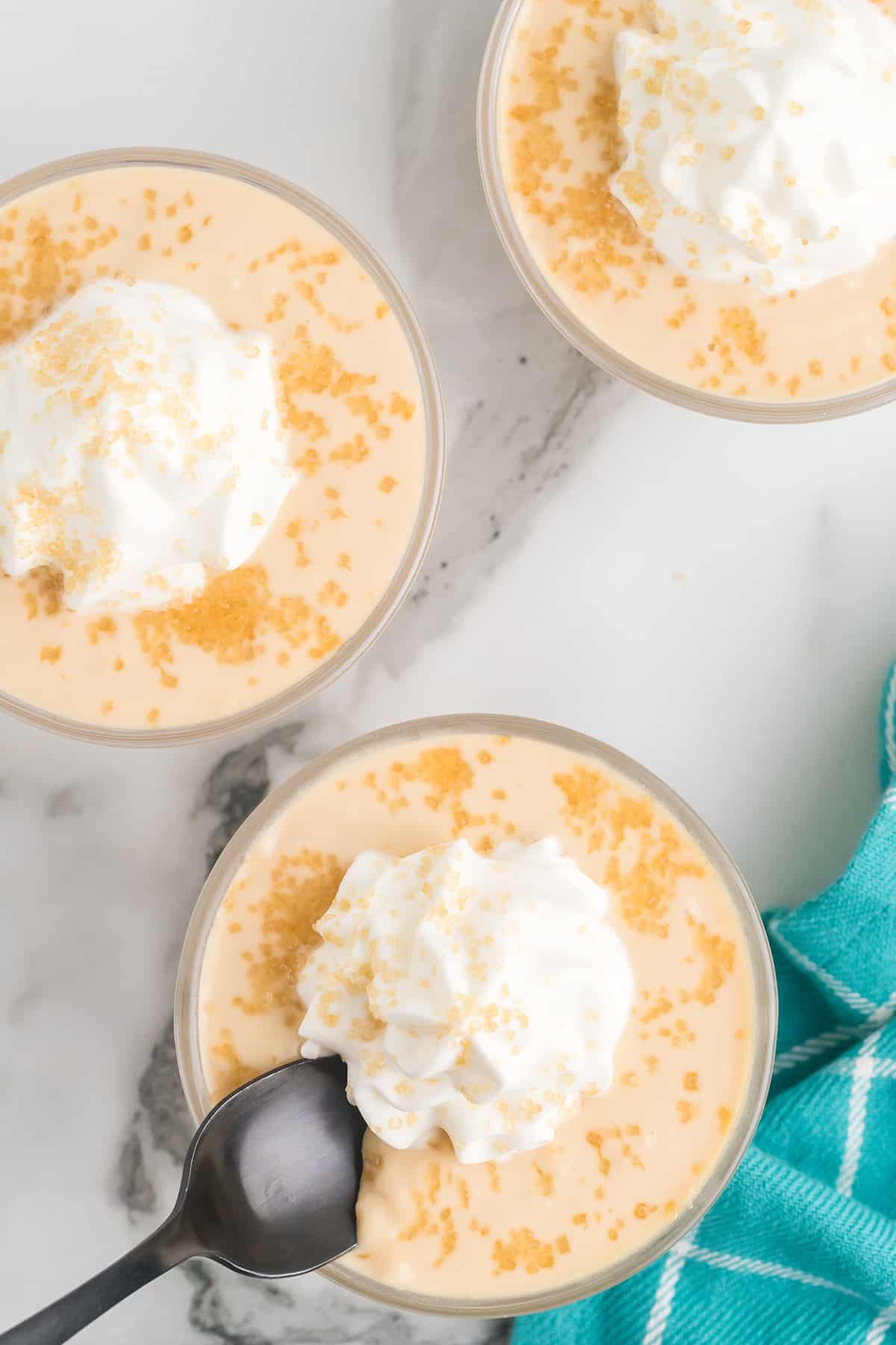 Three dishes filled with butterscotch pudding topped with whipped cream and turbinado sugar.