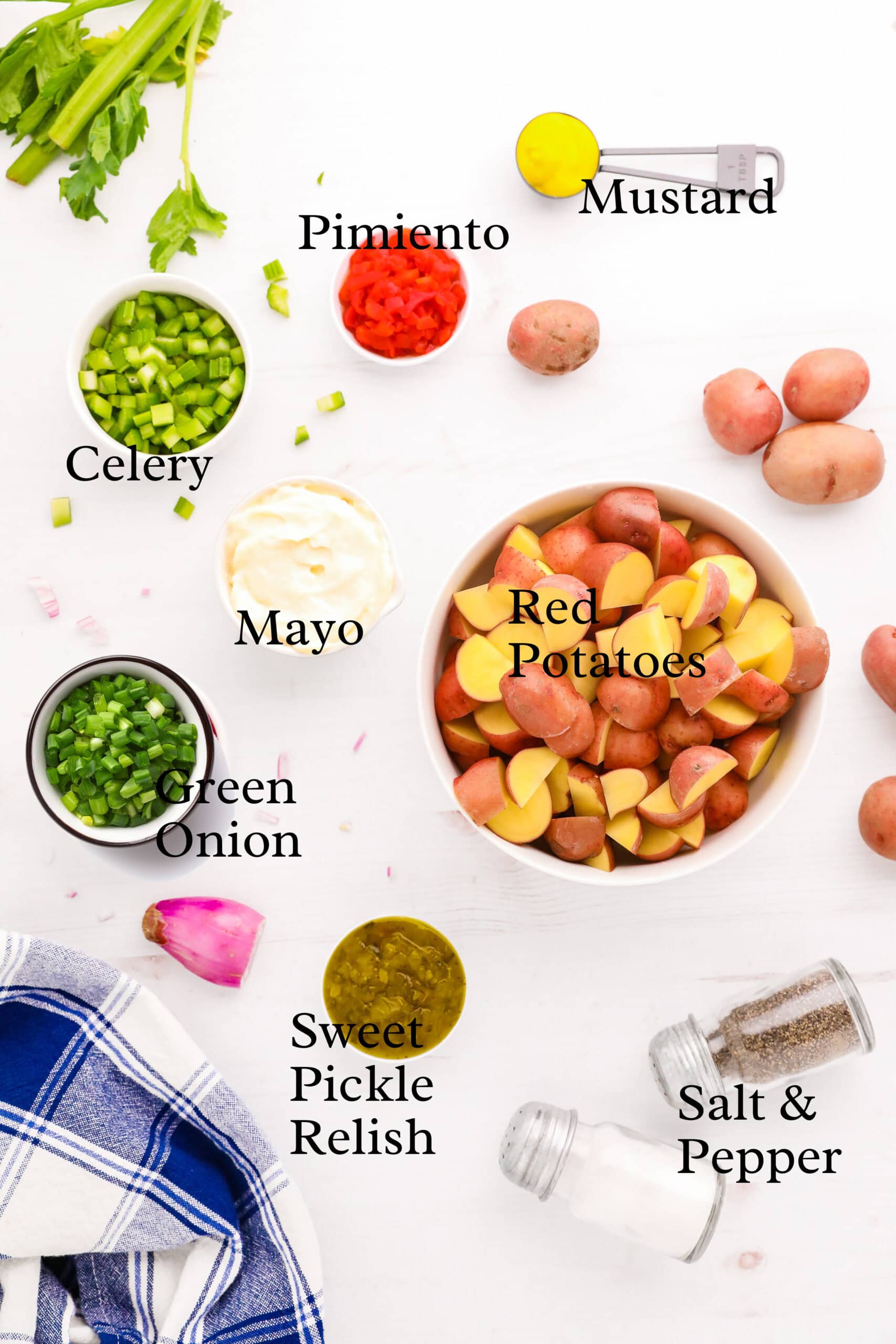 Overhead view of potato salad ingredients: red potatoes, mayo, celery, green onion, pimiento, mustard, relish.