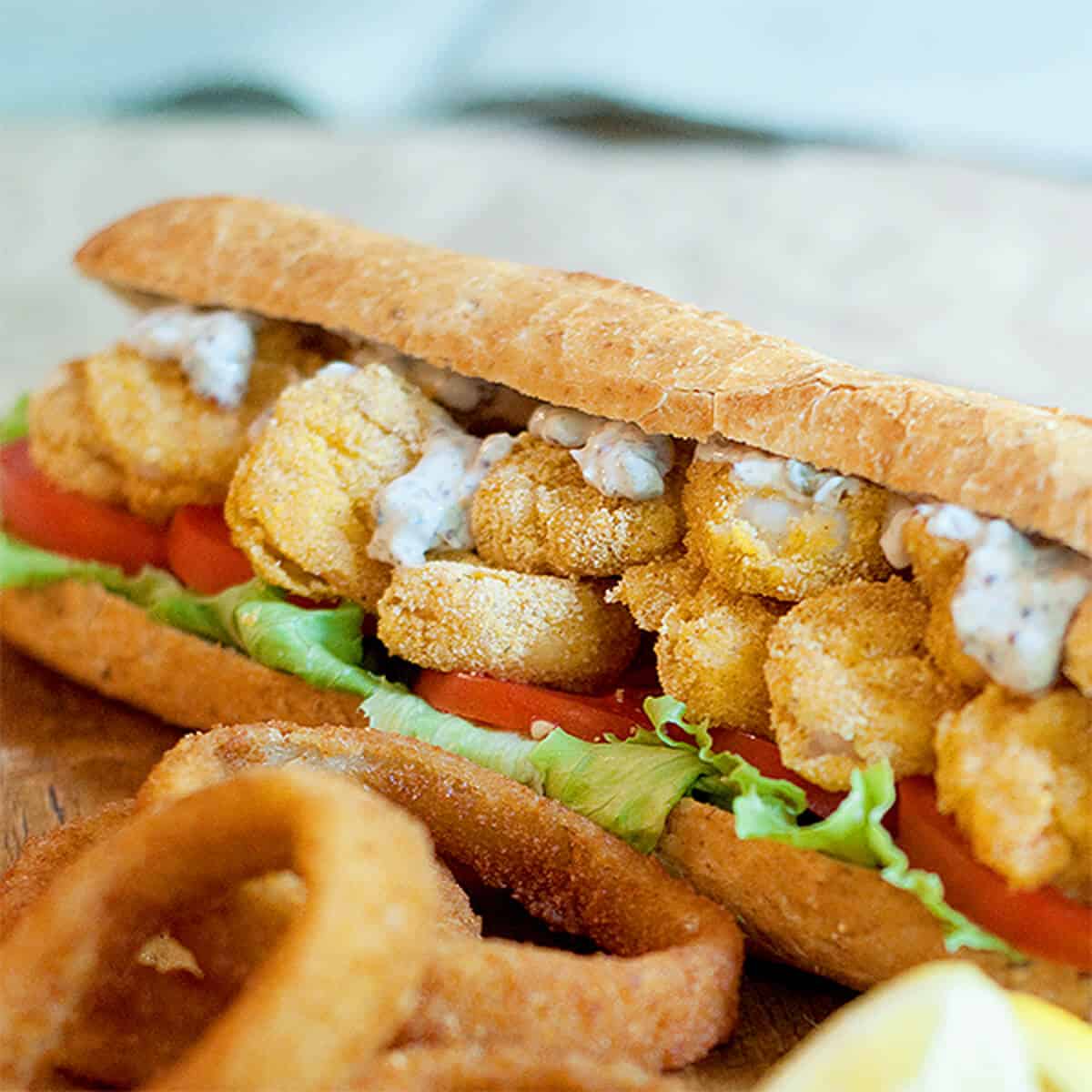 Shrimp po' boy sandwich with onion rings and lemon wedges.