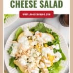 A plate of pear and blue cheese salad with lettuce, almonds, and creamy dressing on a white table.