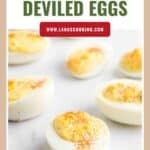 Halved deviled eggs with creamy filling, sprinkled with paprika, on a white surface.