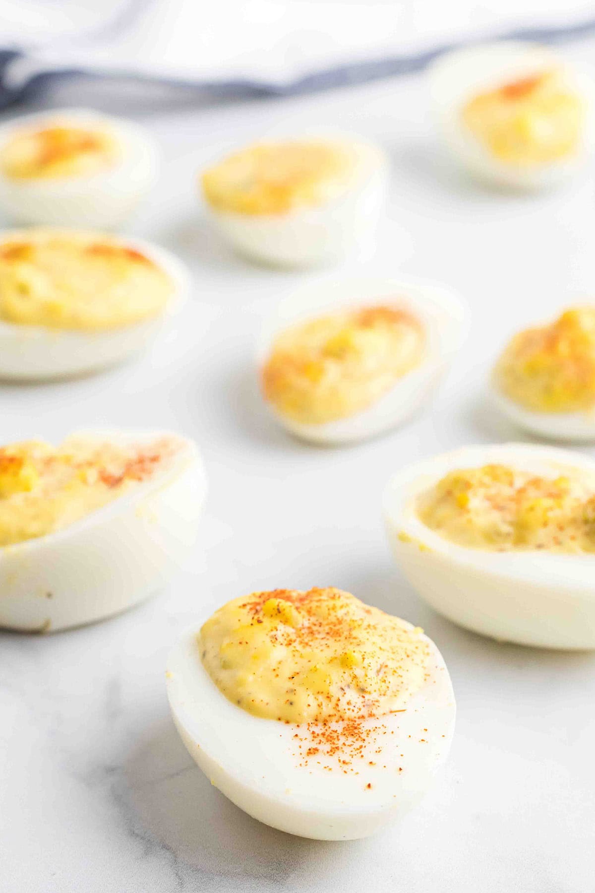 Deviled eggs topped with paprika, arranged on a white surface with a blurred background.