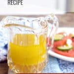 A glass pitcher filled with yellow lemon vinaigrette sits on a table next to a plate of sliced tomatoes and mozzarella. Text reads Lemon Vinaigrette Recipe—get it on Lana’s Cooking.