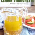 A glass pitcher of yellow lemon vinaigrette sits on a blue cloth with a plate of sliced tomatoes and cheese in the background. Text reads “Easy & Fresh Lemon Vinaigrette lanascooking.com.”.