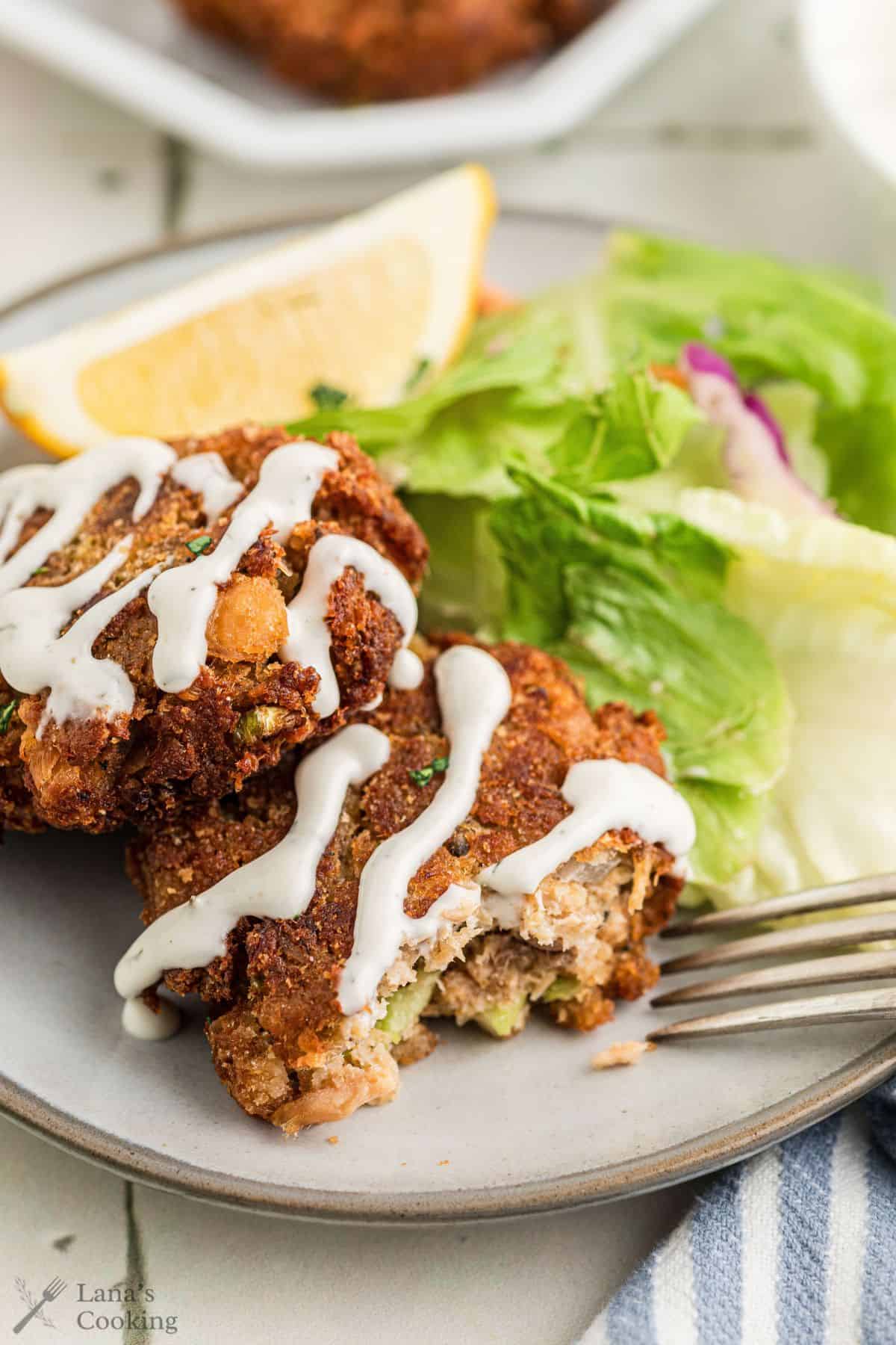 Salmon croquettes on a plate with salad and a wedge of lemon with sauce on top