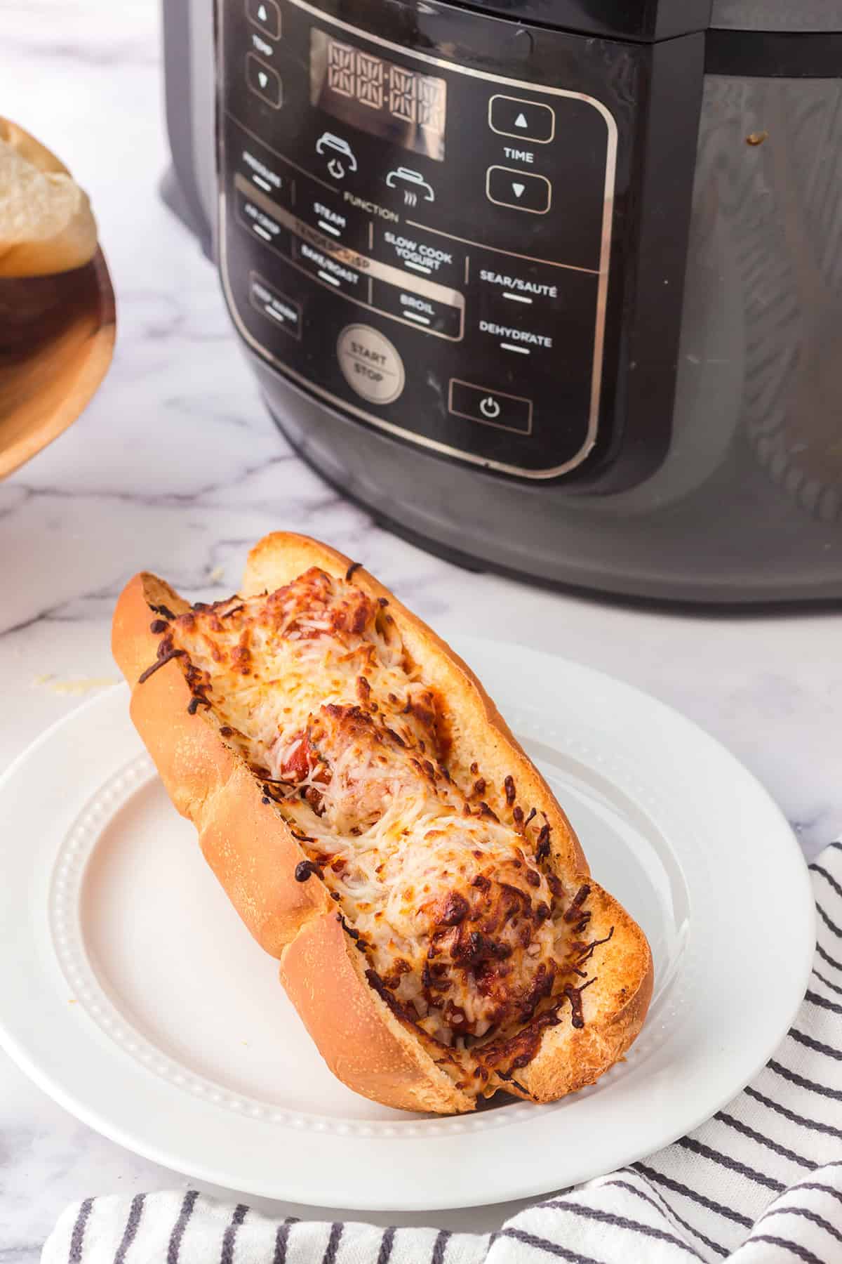 Meatball sub with melted cheese on a white plate in front of an air fryer.
