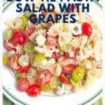 A plate of bow tie pasta salad with red and green grapes, tomatoes, cheese, and herbs.