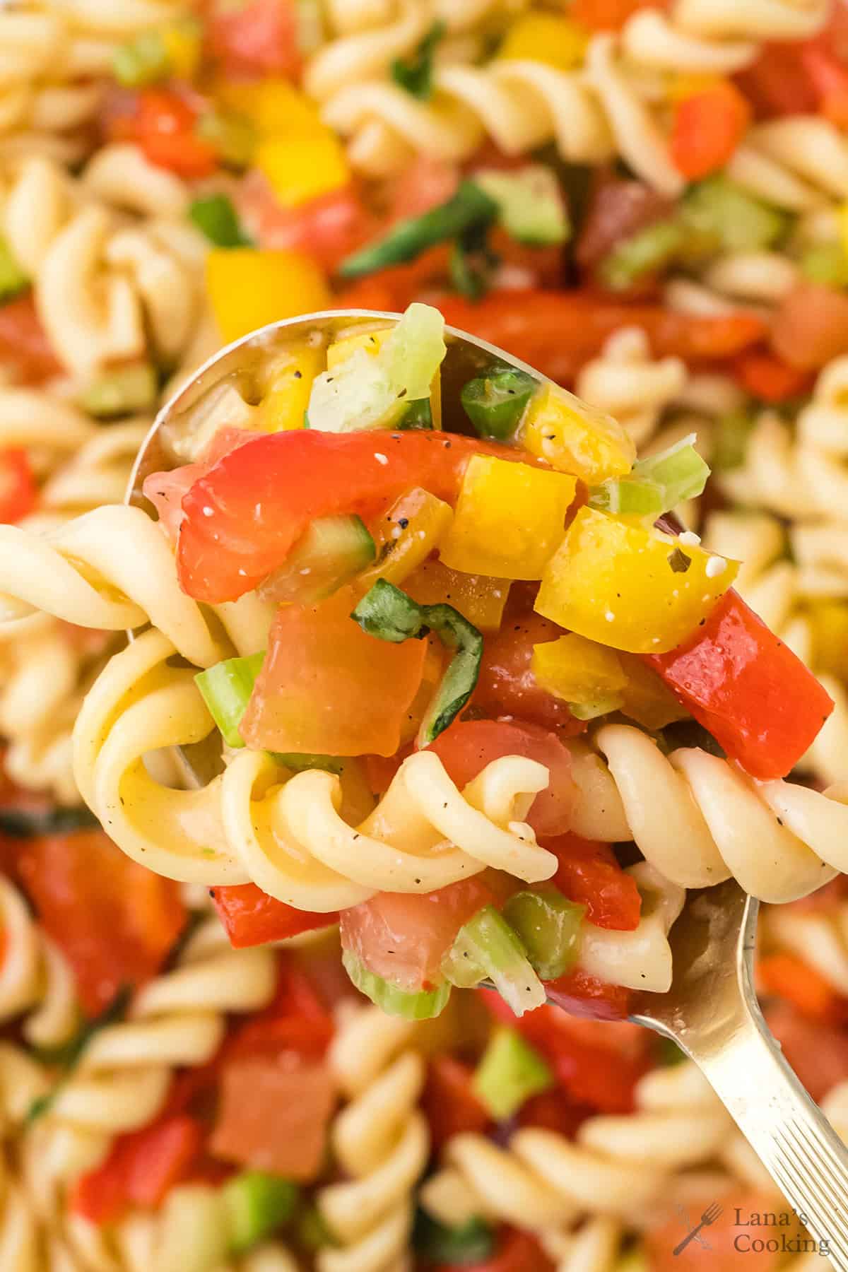 A spoonful of pasta salad with rotini, diced tomatoes, yellow peppers, and herbs.