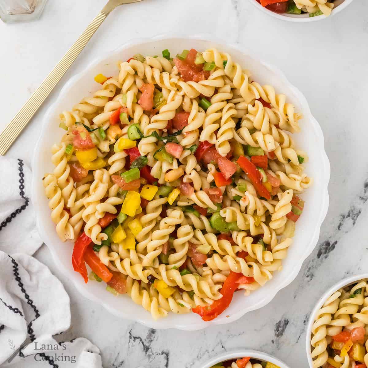 A bowl of rotini pasta salad with tomatoes, peppers, and cucumbers on a marble surface.
