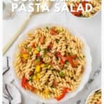 A bowl of pasta salad with vegetables on a marble table, with text promoting summertime pasta salad.