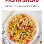 A bowl of colorful pasta salad with tomatoes and peppers on a white surface, perfect for summer parties.