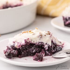 A slice of blueberry pineapple congealed salad with whipped topping and nuts on a white plate, with a spoon beside it.