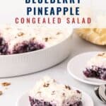 Two plates with slices of blueberry pineapple congealed salad in front of a larger serving dish, with a fork and a striped napkin nearby.