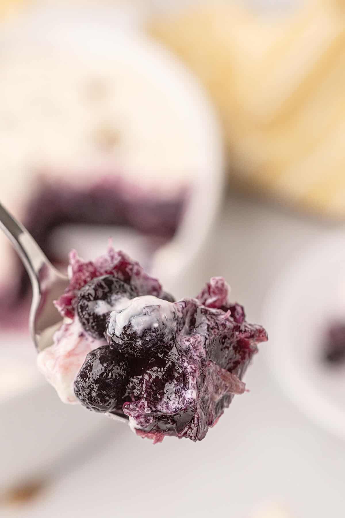 A spoonful of creamy blueberry dessert with whole berries, held above a blurred background.