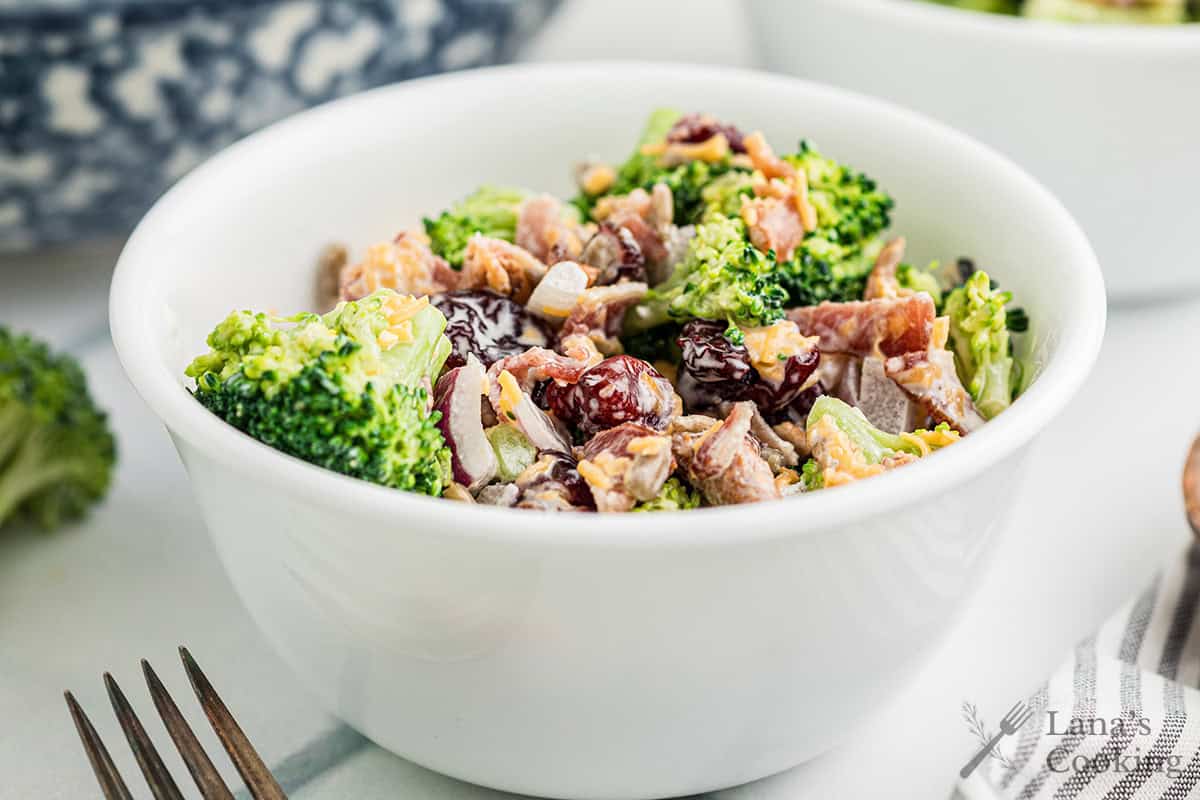 A serving of broccoli salad in a white bowl.