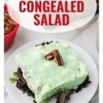 A slice of lime congealed salad with pecans on top, served on lettuce on a white plate.