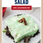 A square slice of green lime congealed salad on lettuce, garnished with pecans.