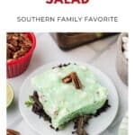 A square of lime congealed salad with pecans sits on lettuce, garnished with a pecan half.