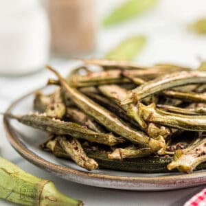 A plate of crispy baked okra chips is served on a ceramic dish, with a blurred background.