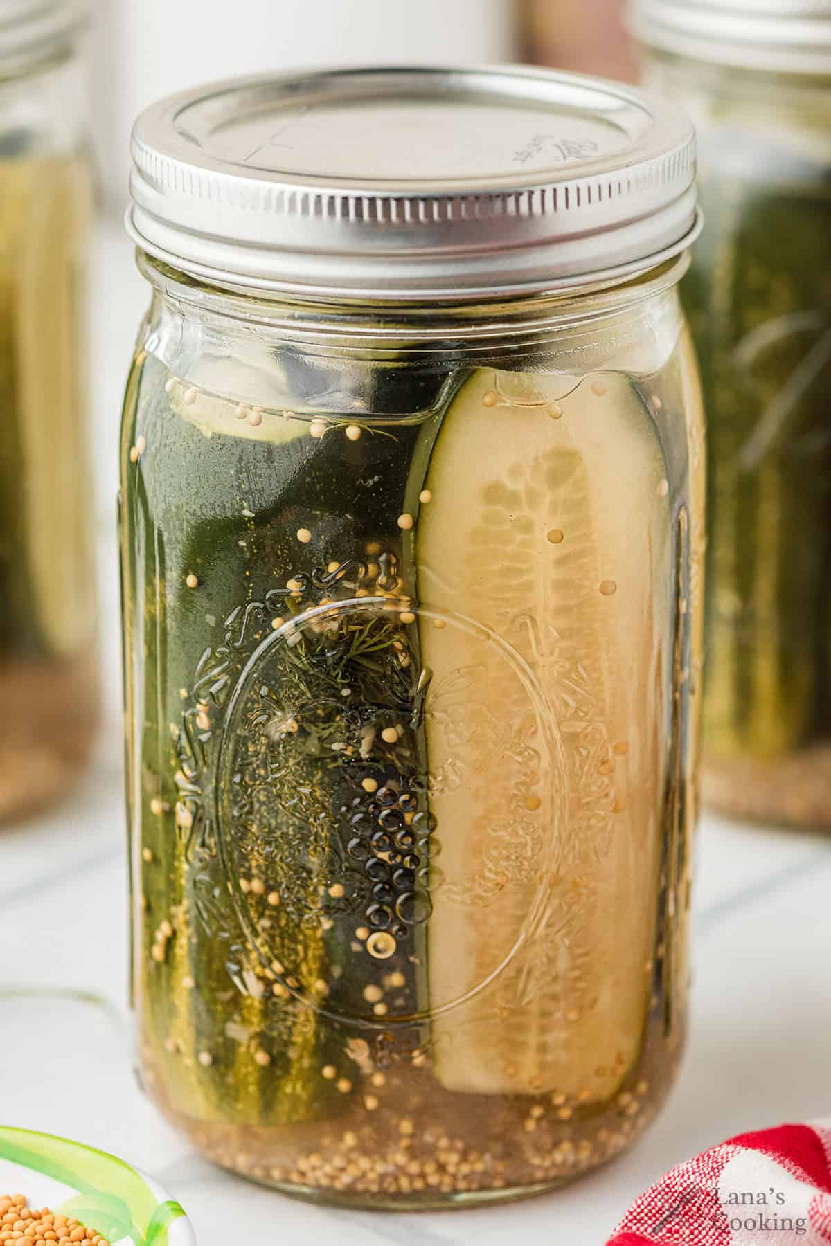 A glass jar filled with Claussen copycat pickles, mustard seeds, and brine, sealed with a metal lid.