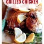 Grilled spatchcocked chicken garnished with lemon wedges and herbs on a wooden board.