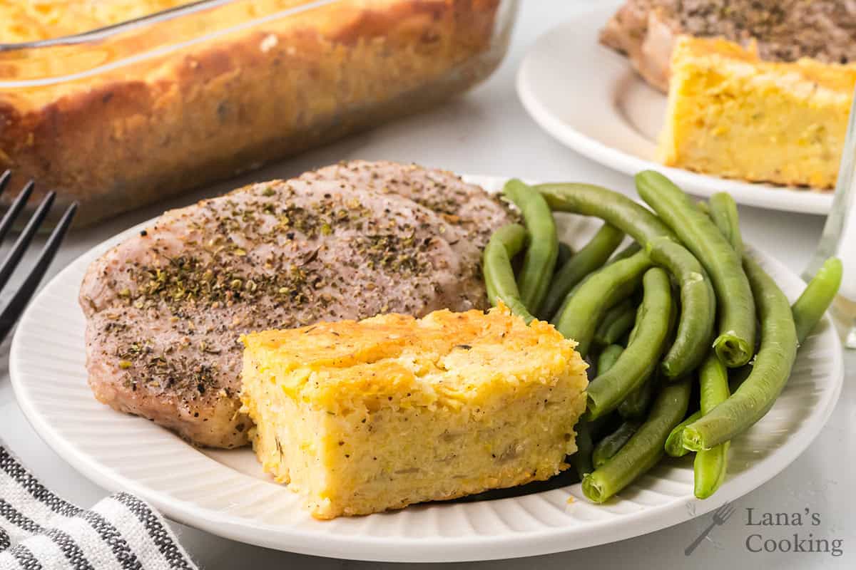 A serving of squash cornbread casserole on a plate with green beans and pork chops.