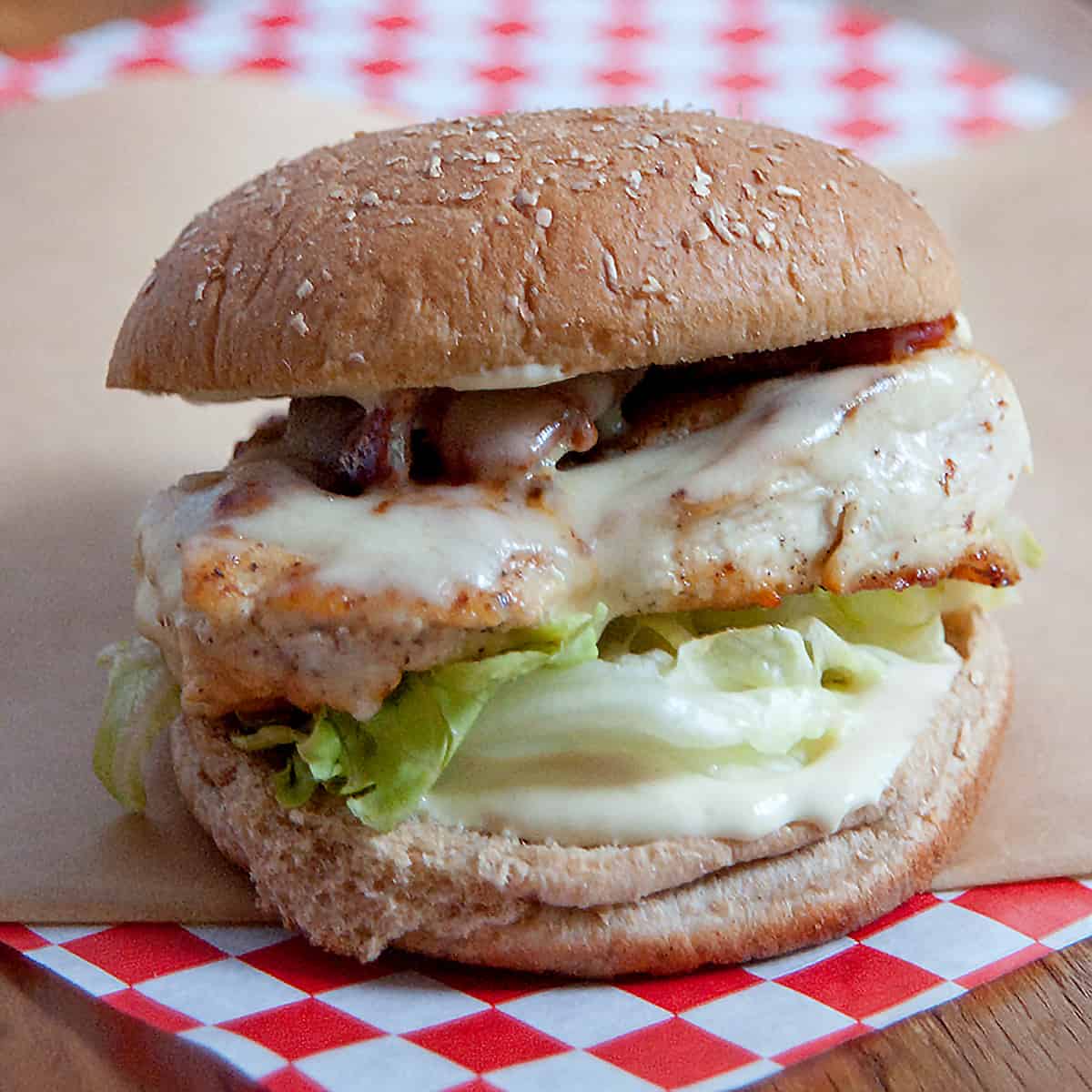 Chicken, bacon, and swiss sandwich on a red and white checked deli paper.