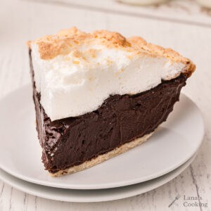 A slice of chocolate pie with fluffy meringue topping on a white plate.