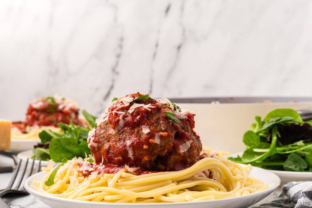 A white plate with spaghetti topped with a jumbo meatball.