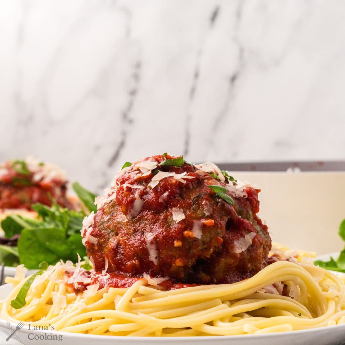 Spaghetti and a jumbo meatball on a plate with parsley on top.