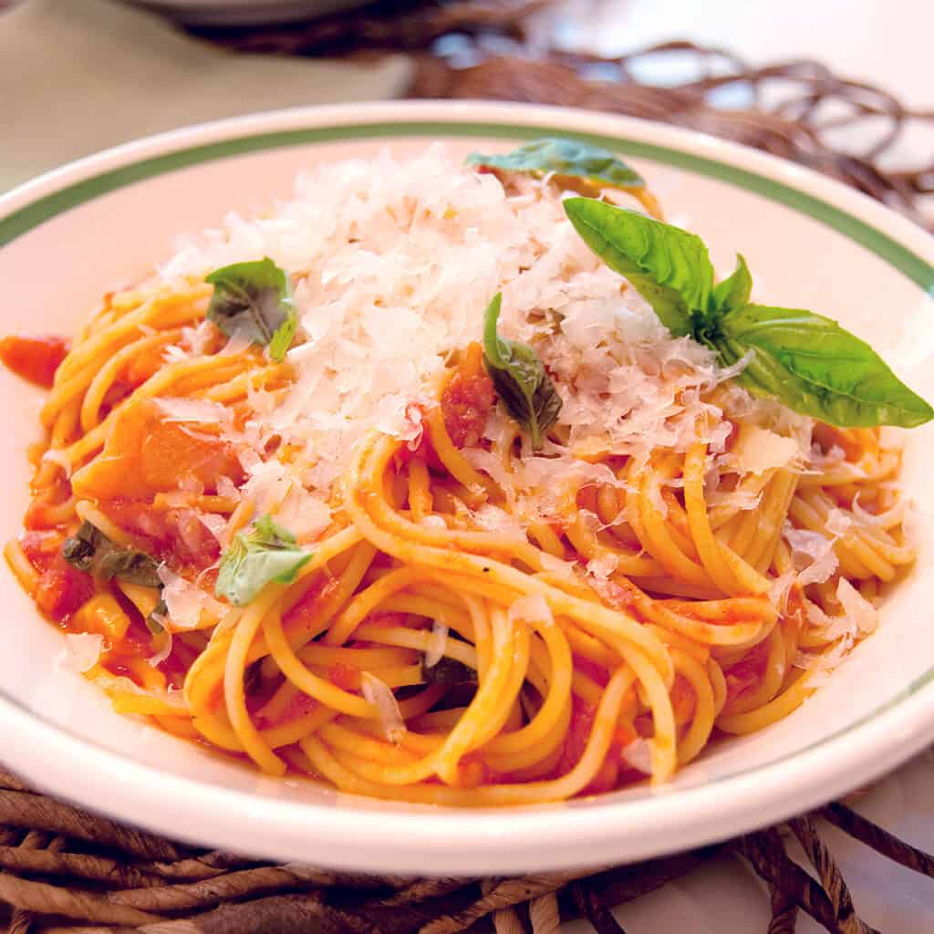 A white dish holding a serving of pasta with tomato basil sauce.