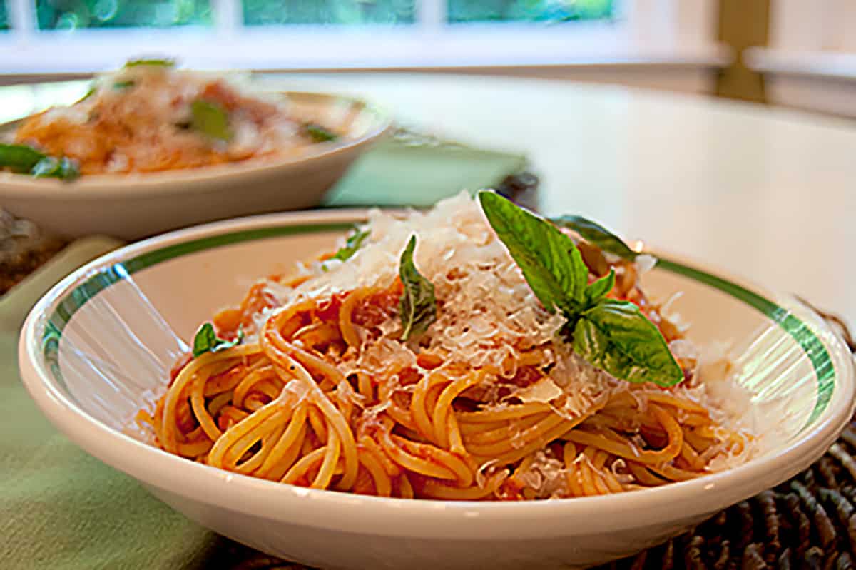 A white dish holding a serving of pasta with tomato basil sauce.