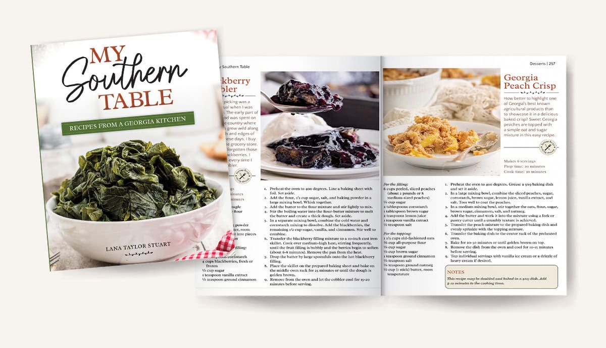 An open cookbook titled My Southern Table shows pages with recipes and photos of blackberry cobbler, biscuits, and Georgia peach crisp. The cover features a bowl of cooked greens.
