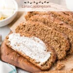 Sliced steakhouse honey wheat bread spread with butter on a wooden board.