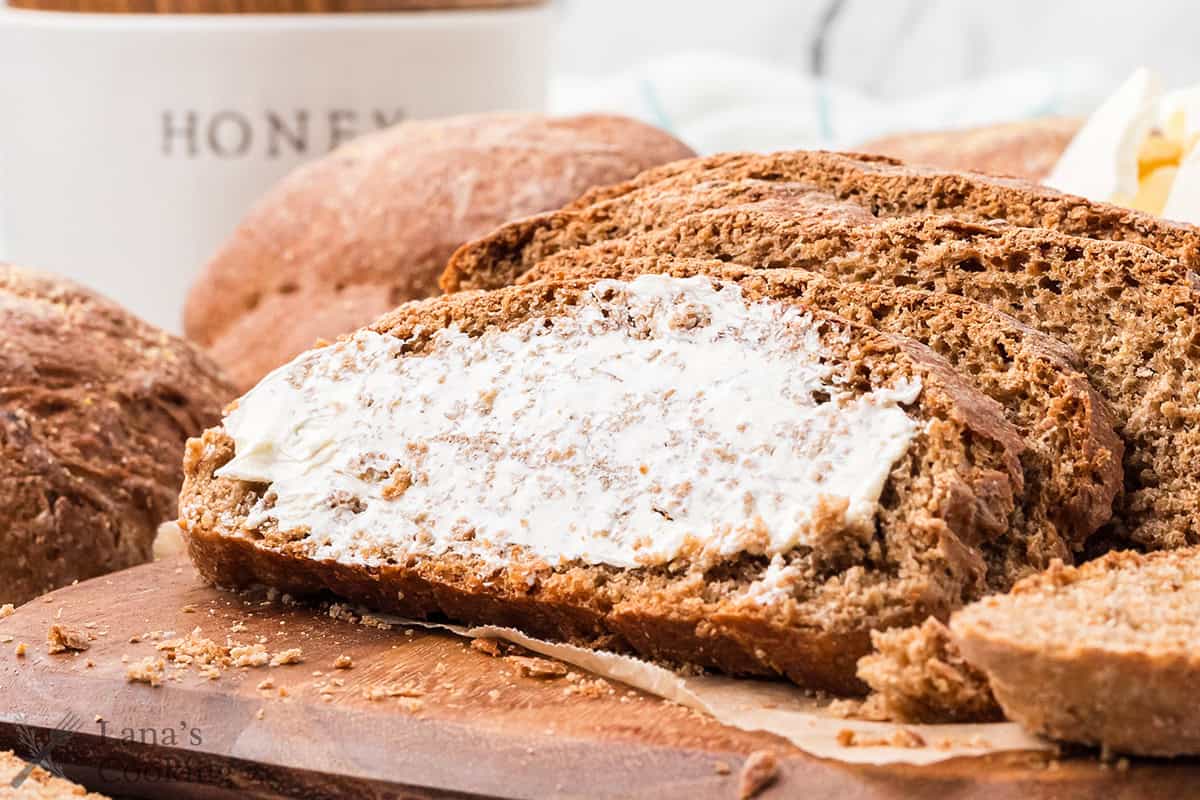 Sliced steakhouse honey wheat bread spread with butter on a wooden board.