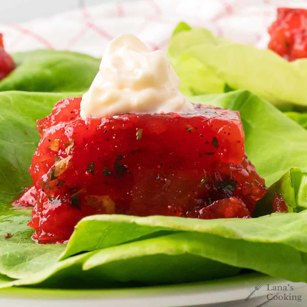 A serving of tomato aspic on a lettuce leaf topped with a dollop of mayonnaise.