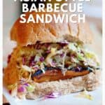 A sandwich with coleslaw, barbecue meat, and a whole wheat bun sits on parchment paper.