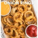 Baked panko onion rings on a tray with bowls of orange dipping sauce and ketchup.