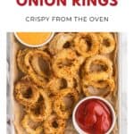A tray of baked panko onion rings with bowls of ketchup and orange dipping sauce on the side.