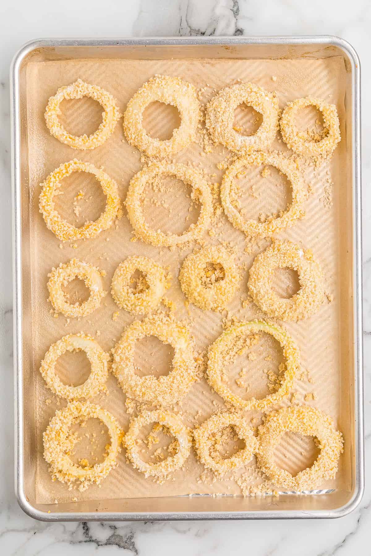 Breaded onion rings on a parchment lined baking sheet.