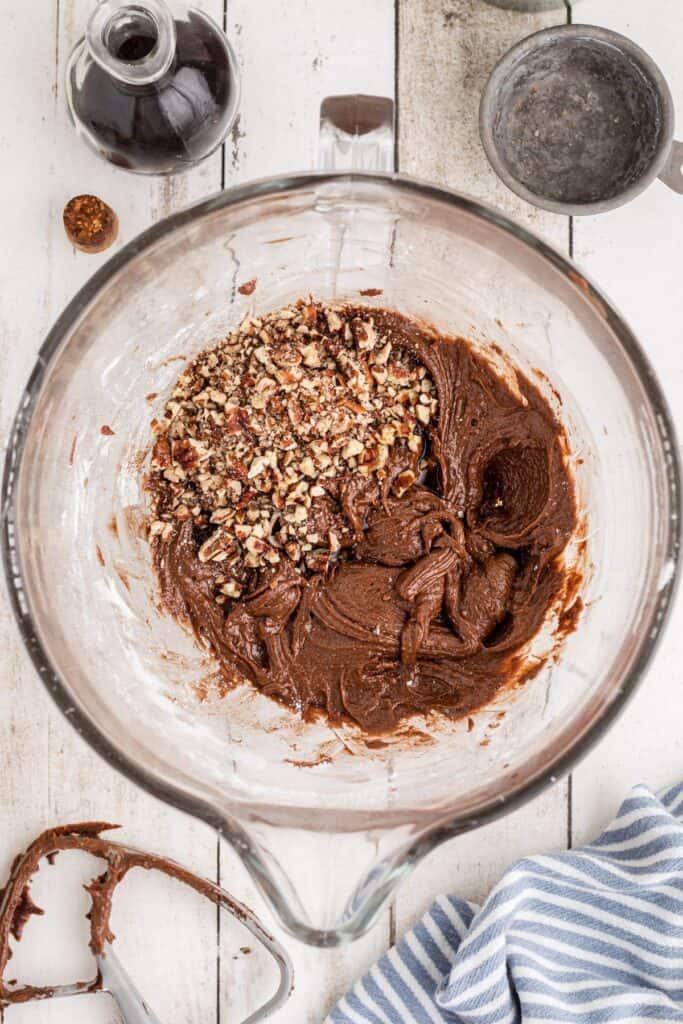 Chopped nuts added to a glass bowl with the brownie batter inside before being mixed.